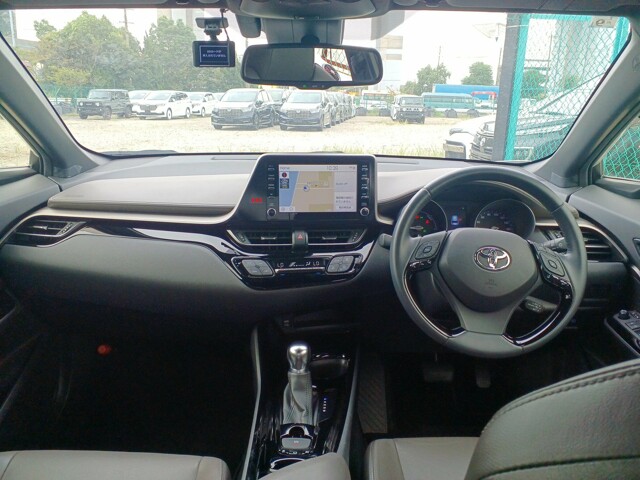 Interior view from the front seat of a right-hand drive Toyota C-HR, showcasing the dashboard layout, steering wheel, and center console infotainment system.